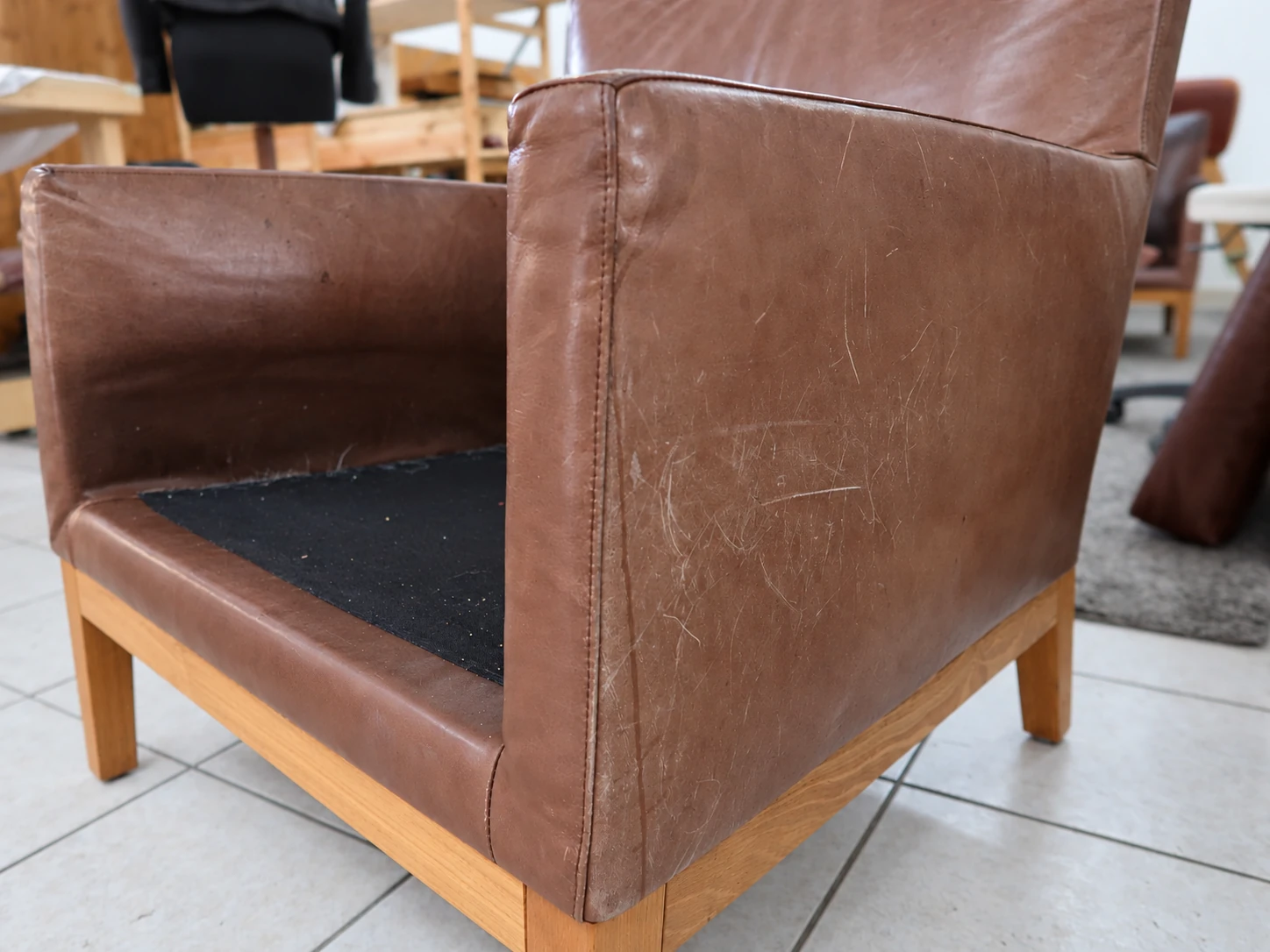 Side view of the brown aniline leather armchair with faded and scratched surfaces before restoration